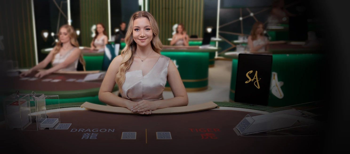 Smiling woman in a red dress seated at a casino table, elegantly presenting playing cards, with gaming tables in the background.
